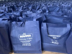 Thanksgiving 2022 bags of food: navy blue cloth bags with the MANNA logo on one side and the sponsor logos on the other